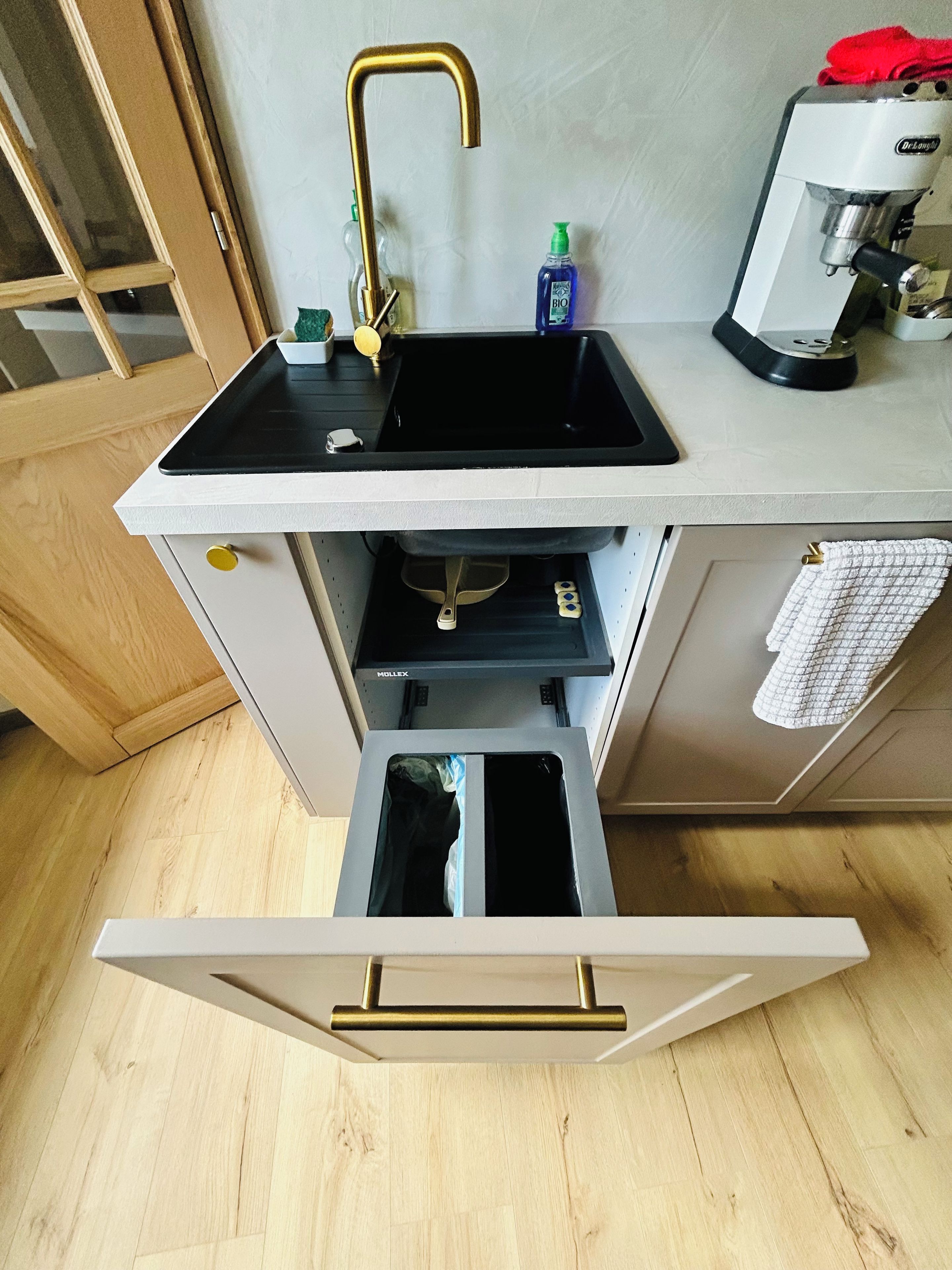 A kitchen with a black sink, a coffee machine, and a drawer with a gold handle.