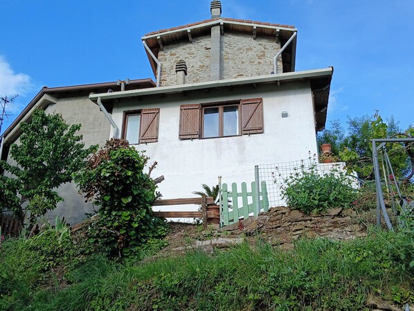 Un edificio de dos pisos con una torre de piedra, contraventanas de madera y fachada blanca.