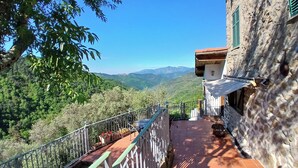 Un balcone con vista su un paesaggio montuoso, un muro in pietra e un pavimento piastrellato.