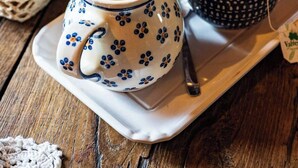 Un tavolo con un teiera, una tazza di tè, un piatto di cibo e un cesto di pane.