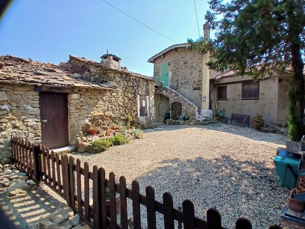 A stone building with a gravel courtyard, a wooden fence, and potted plants. - Cozy Cottage Retreat in Berzi (Bajardo)