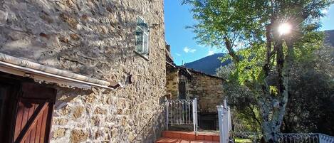 A stone building with a wooden door, a metal gate, and a paved area with a white chair.
