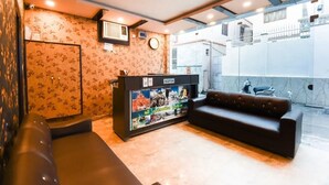 A reception area with a sofa, a reception desk, a clock, and a wall with floral wallpaper. - Hotel Ganga Inn (Haridwar)