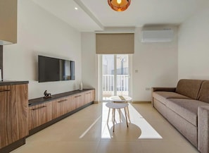 Una sala de estar moderna con un televisor de pantalla plana, un sofá, una mesita redonda y una cocina con armarios de madera.