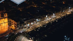 Luchtbeeld van een stadsgezicht 's nachts, met verlichte gebouwen, een opvallende kerk en een oeverpartij met afgemeerde boten.