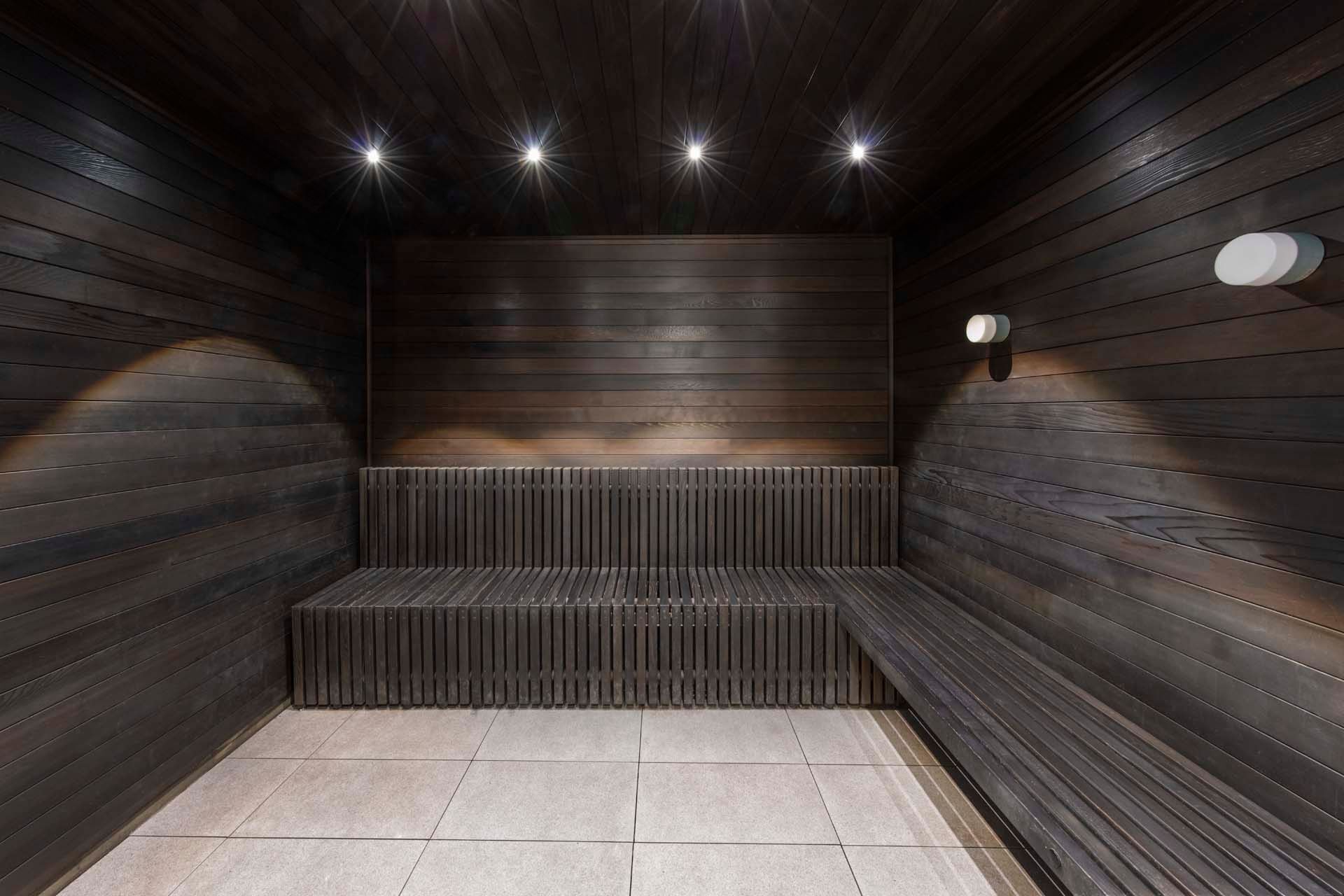 En sauna med trævægge, en bænk og en lampe monteret på væggen.