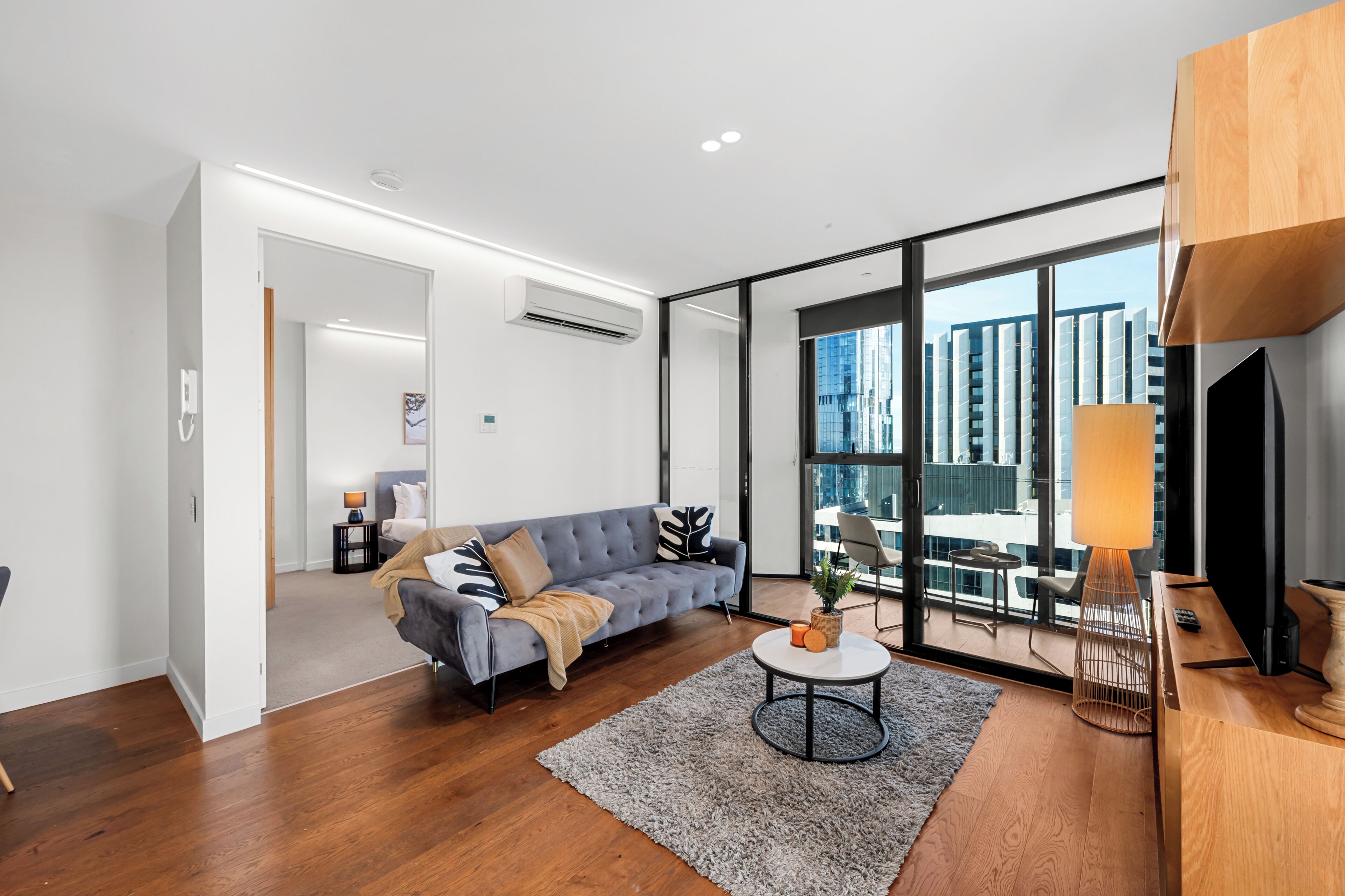 A modern living room with a grey sofa, a round coffee table, and a large window offering a city view.