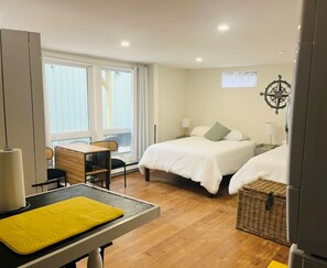 Ein Hotelzimmer mit zwei Betten, einem Schreibtisch, einem Stuhl, einem kleinen Tisch mit gelunder Unterlage, einem Fenster mit Vorhängen und einer Wanddekoration.