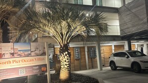 A modern building with a sign for North Pier Ocean Villas, a palm tree, and a white car parked in front. - Brand New Oceanfront 2BR/2BA- Hot Tub, Heated Pool, EV Charger, 2 Parking spots (Carolina Beach)