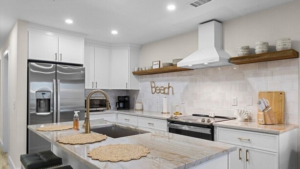 A modern kitchen with white cabinetry, a stainless steel refrigerator, a built-in oven, and a large island with stools. - Brand New Oceanfront 2BR/2BA- Hot Tub, Heated Pool, EV Charger, 2 Parking spots (Carolina Beach)