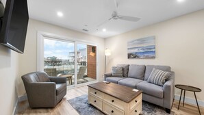 A living room with a sofa, armchair, coffee table, and a TV mounted on the wall. - Brand New Oceanfront 2BR/2BA- Hot Tub, Heated Pool, EV Charger, 2 Parking spots (Carolina Beach)
