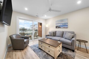 Ein Wohnzimmer mit einer Couch, einem Sessel, einem Couchtisch und einem an der Wand befestigten Fernseher.