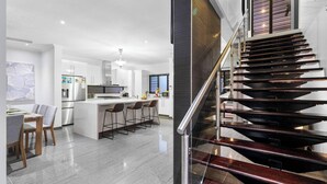 A modern kitchen with a central island, stainless steel appliances, and a dining area with chairs. - Zen Tropica Family Luxury Retreat Pool BBQ (Darwin)