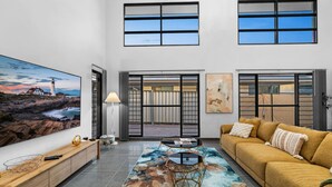 A spacious living room with a large flat-screen TV, a sofa, a coffee table, and a view of the outside through large windows. - Zen Tropica Family Luxury Retreat Pool BBQ (Darwin)