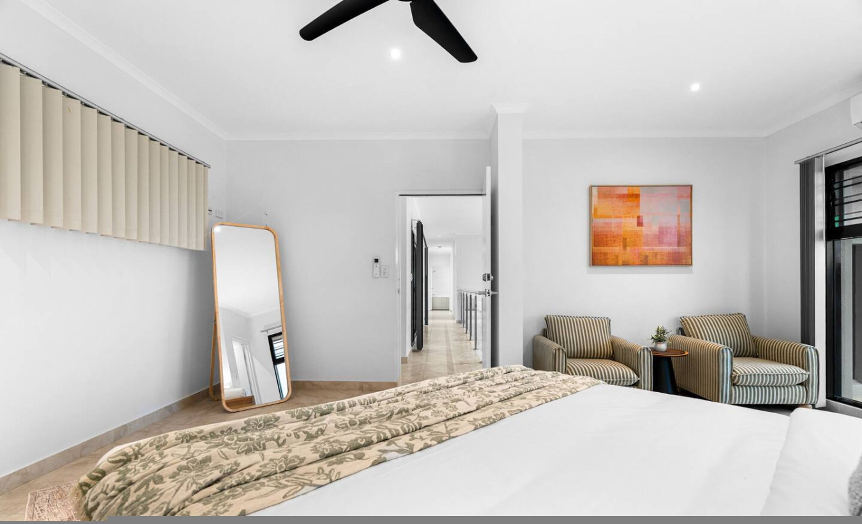 Une chambre d’hôtel avec un lit, un grand miroir, un fauteuil à rayures, une petite table et un tableau accroché au mur.