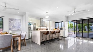 A modern kitchen with a central island, bar stools, and a dining area with a table and chairs. - Zen Tropica Family Luxury Retreat Pool BBQ (Darwin)