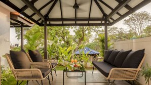 A covered outdoor seating area with wicker furniture and a central table with fruit. - Casa Toledo 4BR in Candolim w Pvt Pool Near Beach (Candolim)