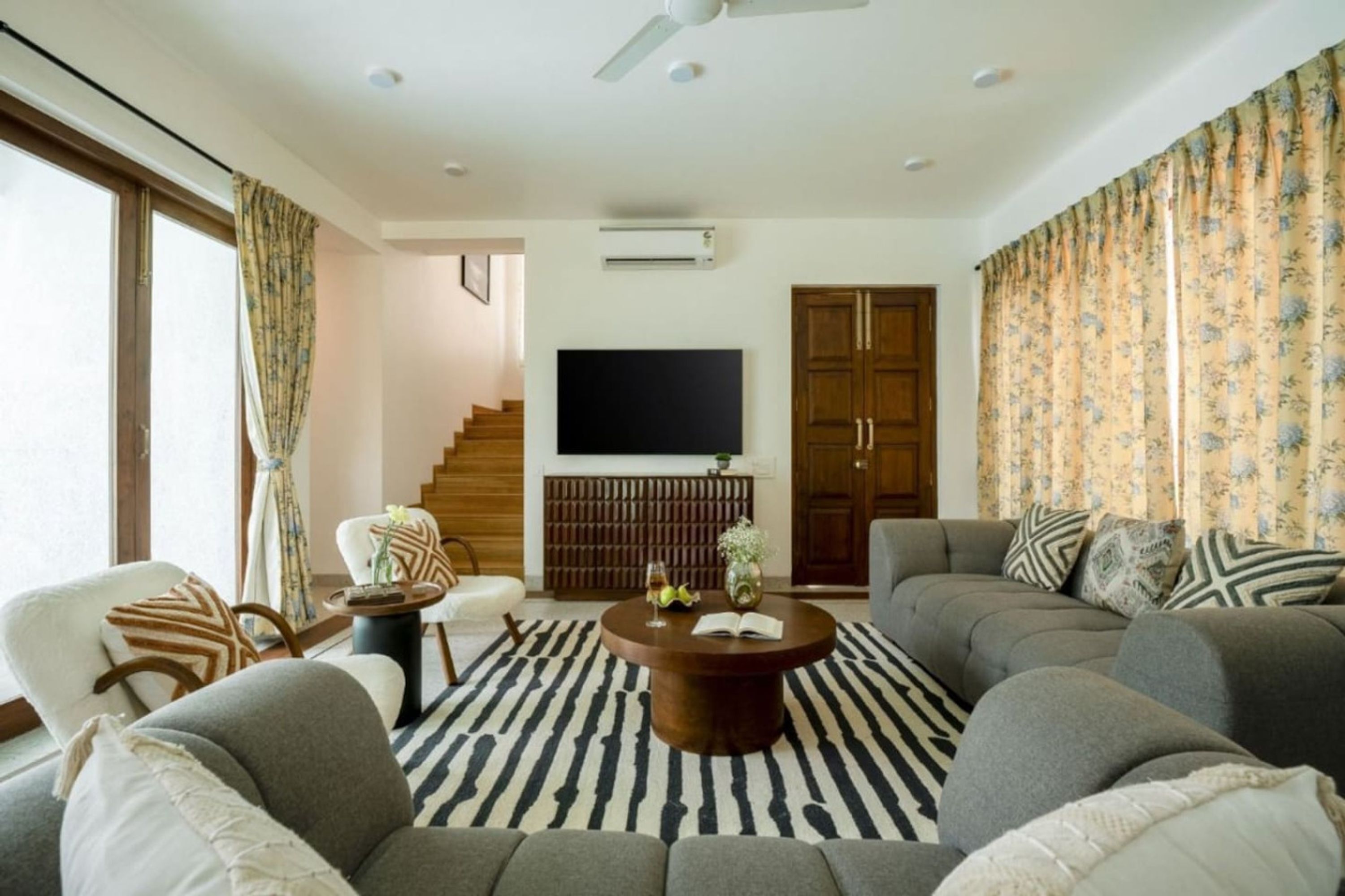A modern living room with a sofa set, a coffee table, a flat-screen TV, and a staircase leading to another level.