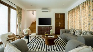 A modern living room with a sofa set, a coffee table, a flat-screen TV, and a staircase leading to another level. - Casa Toledo 4BR in Candolim w Pvt Pool Near Beach (Candolim)