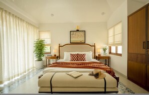A bedroom with a bed, bedside tables, a potted plant, a window with curtains, and a wardrobe. - Casa Toledo 4BR in Candolim w Pvt Pool Near Beach (Candolim)