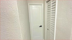 Una puerta blanca con manija negra, una pared blanca con textura y una ventana blanca con persianas horizontales.