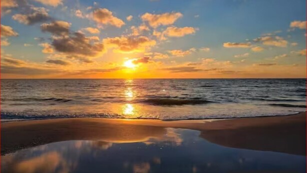 Una playa con atardecer, mar tranquilo y cielo despejado.