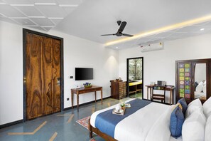 A modern hotel room with a large bed, a ceiling fan, a flat-screen TV, a wooden wardrobe, a desk, and a mirror.