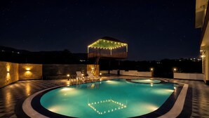 Une piscine dont le fond est illuminé par un motif géométrique, un espace de détente abrité et un ciel étoilé.