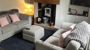A living room with a sofa, ottoman, fireplace, TV, and decorative items. - 2, THE LODGE, TIDESWELL (Tideswell)