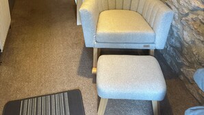 A room with a stone wall, a grey armchair, a matching ottoman, a wooden door, and a white railing. - 2, THE LODGE, TIDESWELL (Tideswell)