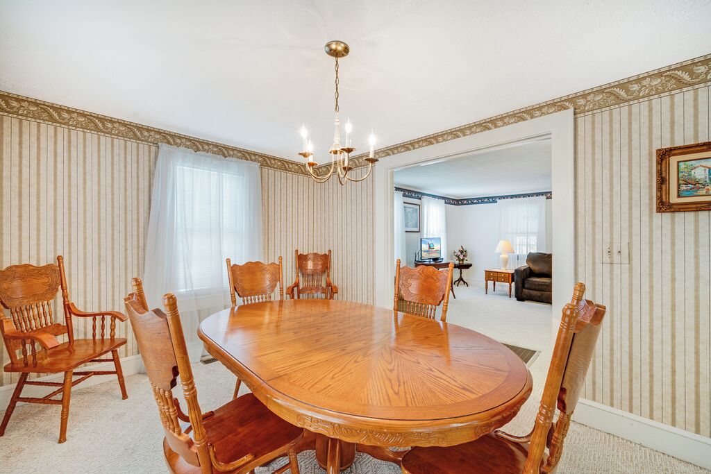 Una sala da pranzo con un grande tavolo di legno e sei sedie, un lampadario e carta da parati a righe.