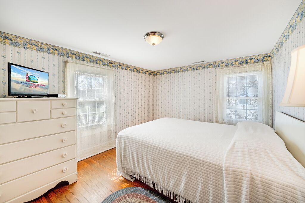 Un dormitorio con cama, cómoda, televisor y papel tapiz estampado.