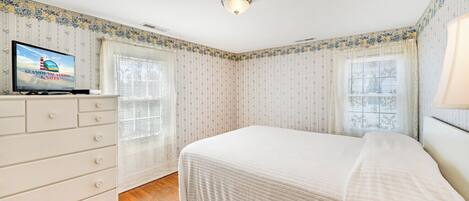 Un dormitorio con cama, cómoda, televisor y papel tapiz estampado.