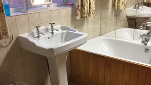 A bathroom with a pedestal sink, a bidet, a bathtub, and a mirror above the sink. - Wansley Manor (Birmingham)