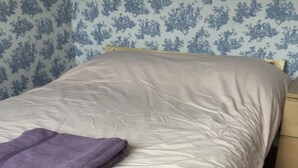 A bed with a white mattress and a purple blanket, a wooden headboard, and a patterned wallpaper background. - Wansley Manor (Birmingham)