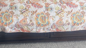 Una cama con colcha estampada con motivos florales, cabecero de madera y dos mesitas de noche con lámparas y un reloj.
