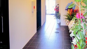 A hallway with a tiled floor, a door on the left, and potted plants on the right. - Hotel Livemax Budget Nagoya Taiko Doriguchi (Nagoya)