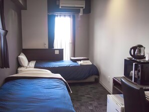 Quarto de hotel com duas camas, uma mesa com chaleira e uma janela com cortinas.