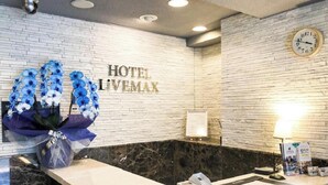 A hotel reception area with a white brick wall, a clock, and a floral arrangement. - Hotel Livemax Budget Nagoya Taiko Doriguchi (Nagoya)