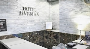 Um hall de hotel com uma recepção de mármore, um relógio e uma placa na parede que diz 'HOTEL LIVEMAX'.