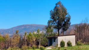 Un edificio pequeño con techo inclinado, rodeado de árboles y un paisaje montañoso.