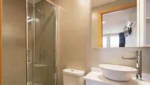 Un baño moderno con ducha de vidrio, inodoro blanco y un lavabo de pedestal grande.