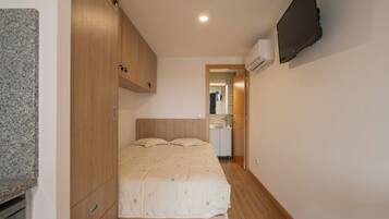 A bedroom with a bed, wooden wardrobe, built-in air conditioning unit, and a television mounted on the wall.