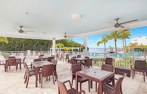Une terrasse extérieure avec des tables et des chaises, des ventilateurs de plafond et une vue sur la mer.