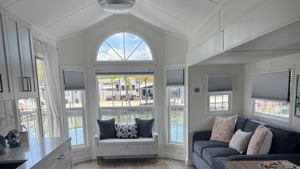 A spacious living area with a large window, a sofa, a coffee table, and a kitchen area with cabinets and a countertop. - Coral Dolphin Cottage- Waterfront tiny home getaway in Key Largo (Key Largo)