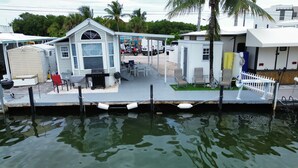 A waterfront property with a covered patio, outdoor seating, and a small building with a garage. - Coral Dolphin Cottage- Waterfront tiny home getaway in Key Largo (Key Largo)