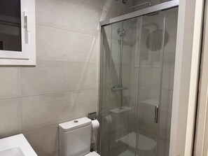 A bathroom with a glass-enclosed shower, a toilet, and a white sink.