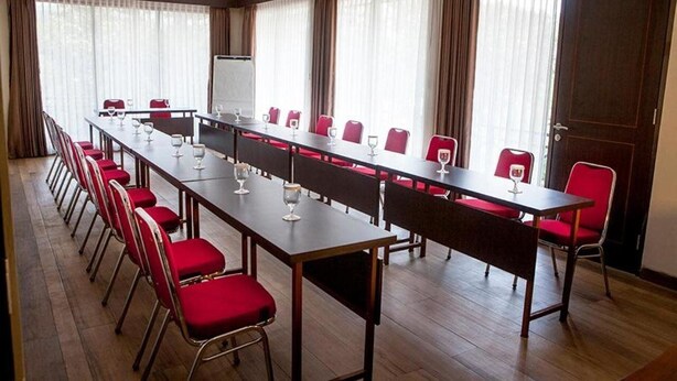 A conference room with a long table, red chairs, and a whiteboard. - Villa Sawah Hotel and Resort (Megamendung)