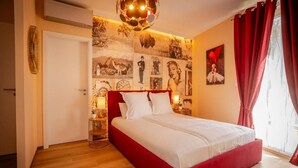 Ein Schlafzimmer mit einem roten Bett, einer Wand mit verschiedenen Bildern, einer Tür und einem Fenster mit roten Vorhängen.