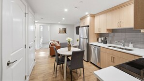 A modern kitchen with wooden cabinets, stainless steel appliances, and a dining area with a white table and chairs. - Luxury 2bedroom Suite With Park Views in Calgary (Calgary)